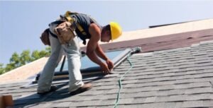“Professional roofing contractor working on a residential or commercial roof. The contractor is wearing safety gear, including a helmet and harness, and using tools to install, repair, or inspect shingles, tiles, or metal roofing panels.