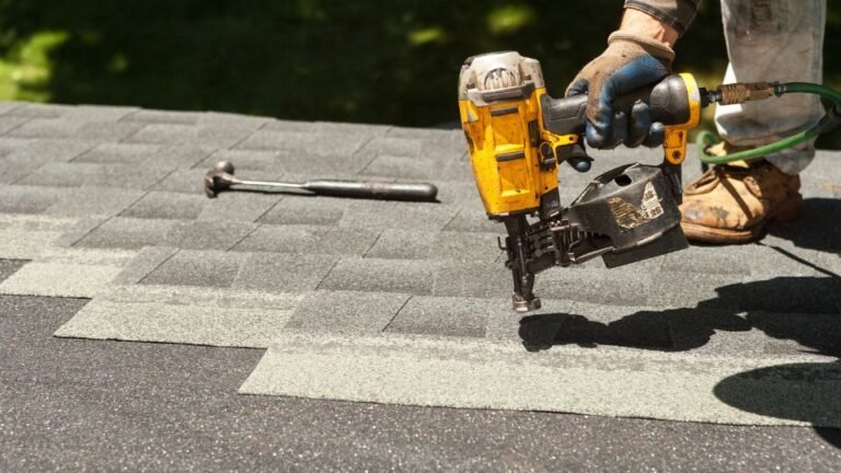 A man is using a nail gun to install roofing materials on top of a house. Wearing safety gear, he secures shingles in place with precision, showcasing the process of modern roof installation and the use of power tools for efficiency.