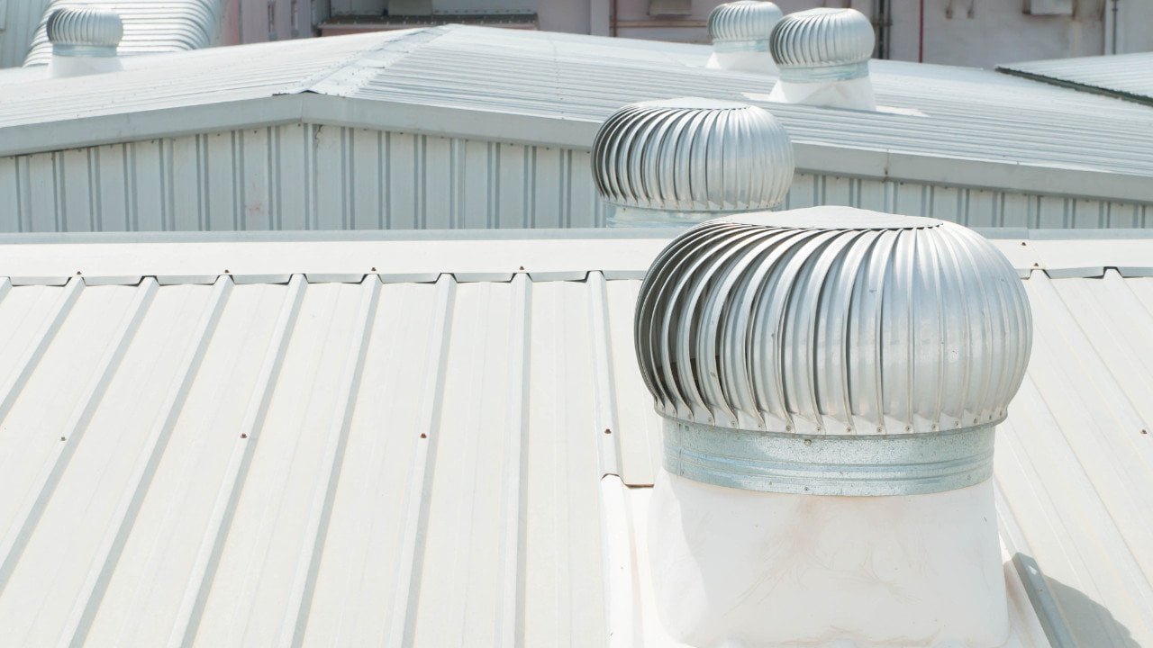 A metal roof featuring a metal vent installed on top for proper ventilation. The reflective roof panels are arranged in neat rows, while the vent provides airflow to regulate temperature and moisture inside the house. The setup highlights durability and efficiency of modern roofing systems.