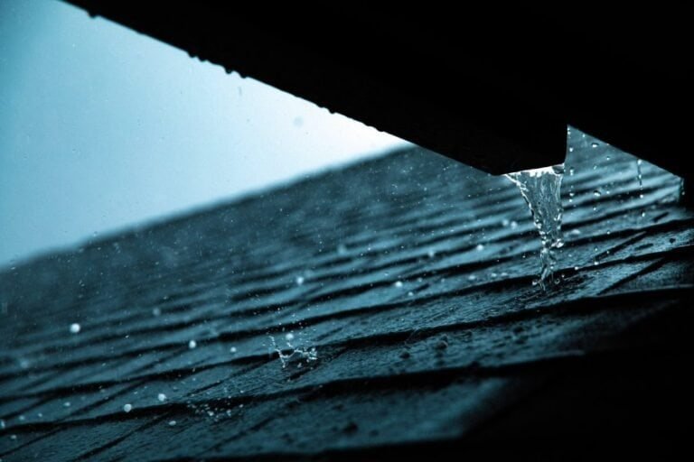 Raindrops falling and collecting on the surface of a roof. The droplets glisten as they land on the roofing material, highlighting the effects of rainfall on the structure and the importance of proper water drainage systems.