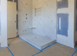A bathroom under renovation featuring blue painter’s tape on the walls, indicating areas being prepared for painting or tiling. The space includes a shower, a sink, and other standard bathroom fixtures. The scene highlights ongoing construction or remodeling work.