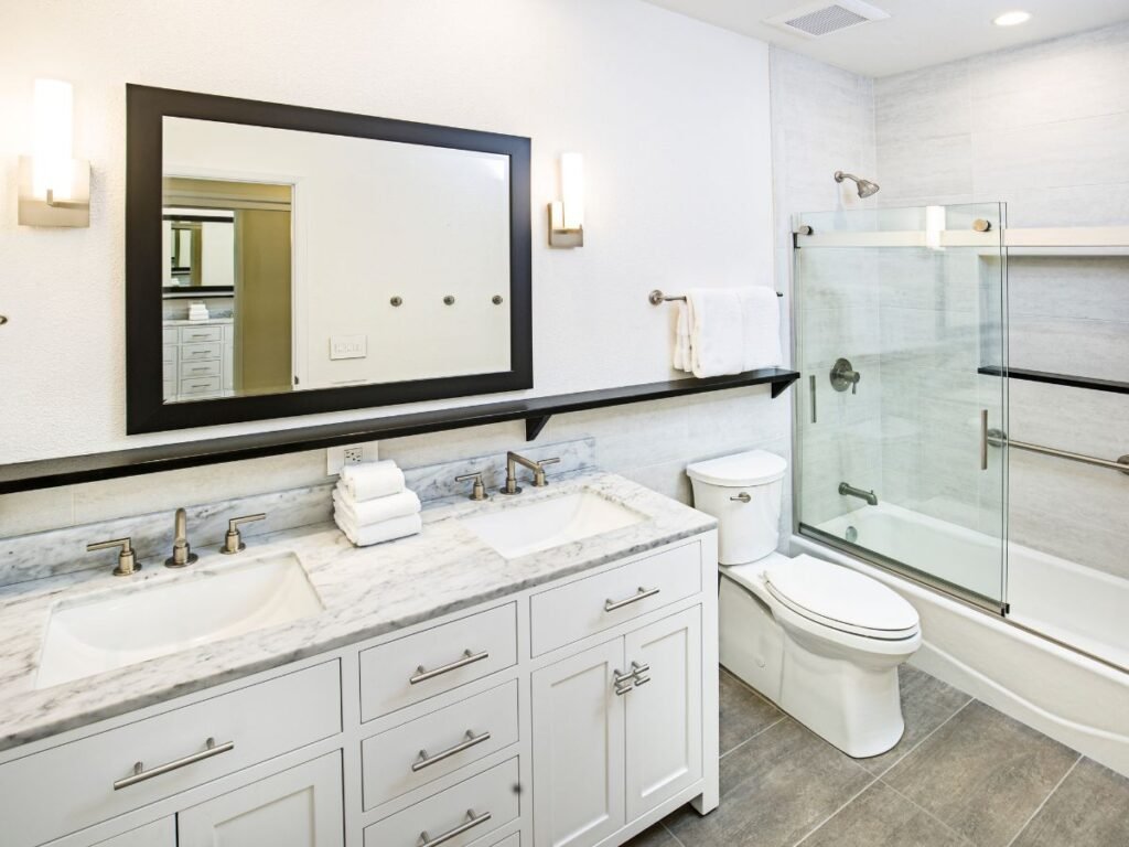 A compact bathroom featuring a shower with a glass or tiled enclosure, a white toilet, and a modern sink with a polished countertop. The space is designed with neutral tones and clean lines, creating a functional and contemporary atmosphere. Lighting highlights the fixtures and adds a sense of openness to the room.