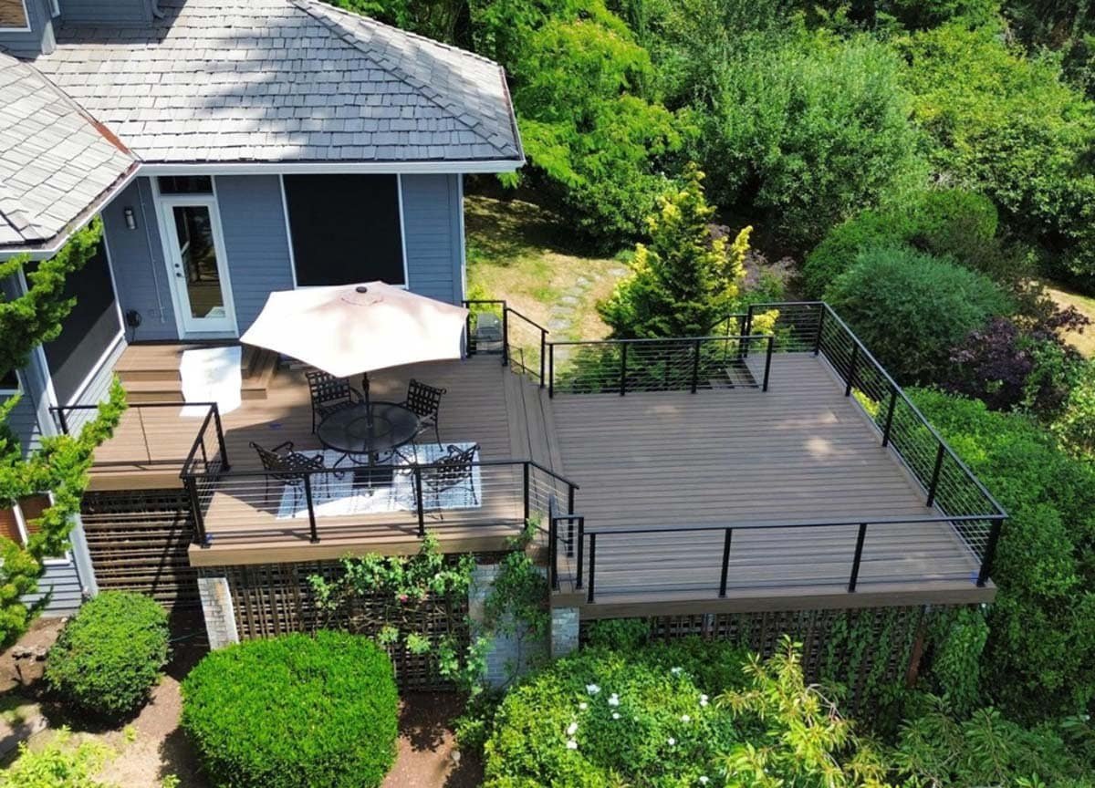 An aerial view of a wooden deck featuring a patio area with a table and chairs arranged for outdoor dining. The deck is surrounded by railings and overlooks a landscaped yard. The patio table has seating for several people, making the space inviting for gatherings and relaxation.