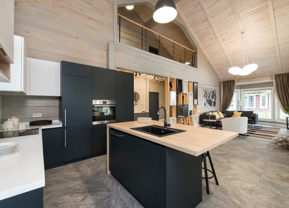 A modern kitchen featuring sleek black cabinets paired with warm wood flooring. The countertops are minimalist, and stainless steel appliances complement the contemporary design. Natural light streams into the space, highlighting the contrast between the dark cabinetry and the rich wood floors, creating a stylish and inviting atmosphere.