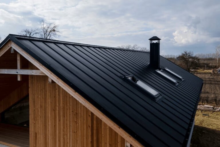 A charming house featuring a dark black roof and a classic chimney. The exterior has clean lines, light-colored walls, and windows with decorative frames. The house is surrounded by a well-maintained yard, giving it a cozy and welcoming appearance.