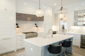 A modern kitchen featuring crisp white cabinets and a luxurious marble island with a polished countertop. The kitchen is bright and airy, with contemporary appliances, pendant lighting above the island, and a clean, minimalist design that combines elegance with functionality.