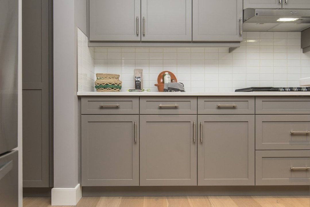 A modern kitchen featuring sleek gray cabinets paired with warm wooden floors. The kitchen includes contemporary appliances, clean countertops, and minimalist fixtures, creating a cozy yet stylish atmosphere that blends modern design with natural textures.