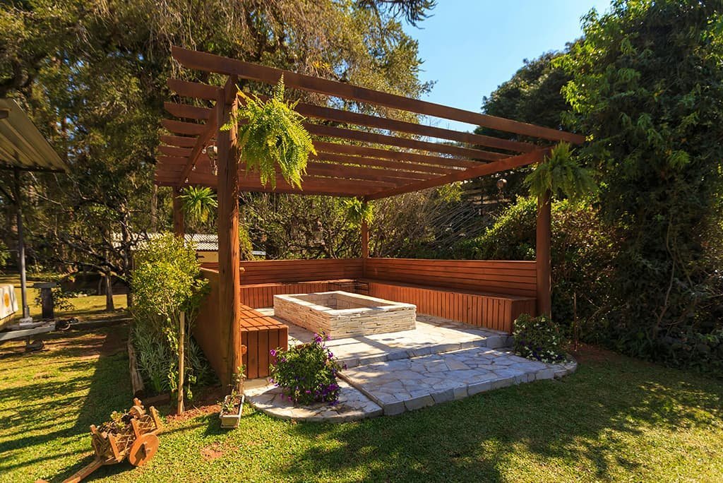 A backyard featuring a wooden pergola providing partial shade over a hot tub. The hot tub is surrounded by decking or patio flooring, and the backyard may include plants, grass, or outdoor furniture. The scene creates a relaxing and inviting outdoor space for leisure and socializing