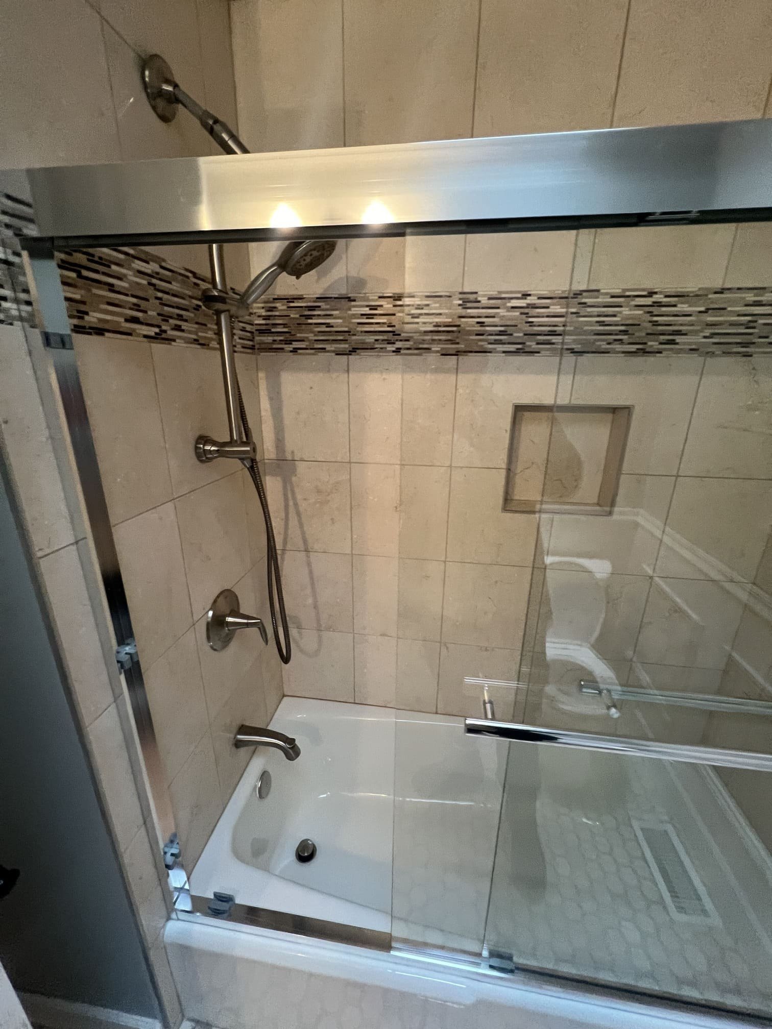 A bathroom featuring a shower enclosed with a glass door and a toilet positioned nearby. The shower area has tiled walls, and the bathroom is clean, organized, and well-lit. The layout is functional, combining bathing and toilet facilities in a compact space.