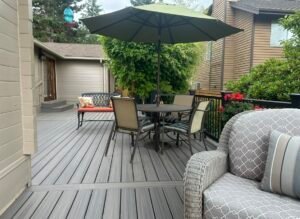 An outdoor patio featuring a table surrounded by several chairs, arranged for dining or relaxation. The patio surface is made of stone, tile, or wood, and sunlight casts natural shadows over the seating area. The setup creates a cozy and inviting space for outdoor gatherings or meals.