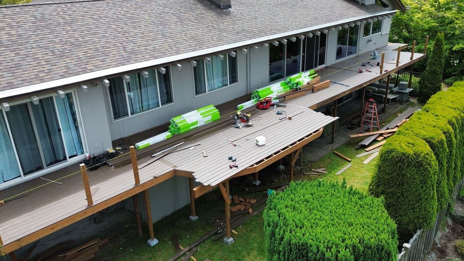 A residential house featuring a wooden deck with decking boards forming the outdoor platform. The deck extends from the house, providing space for outdoor activities or furniture. The surrounding yard and landscaping frame the property, highlighting its exterior features.