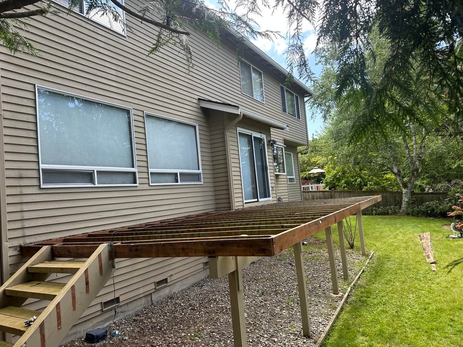 A home with an unfinished wooden deck frame, stairs, and green lawn in the backyard under a cloudy sky.