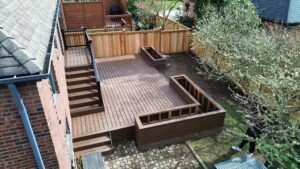 Aerial view of a multi-level wooden deck with benches and stairs in a fenced backyard outdoor space.
