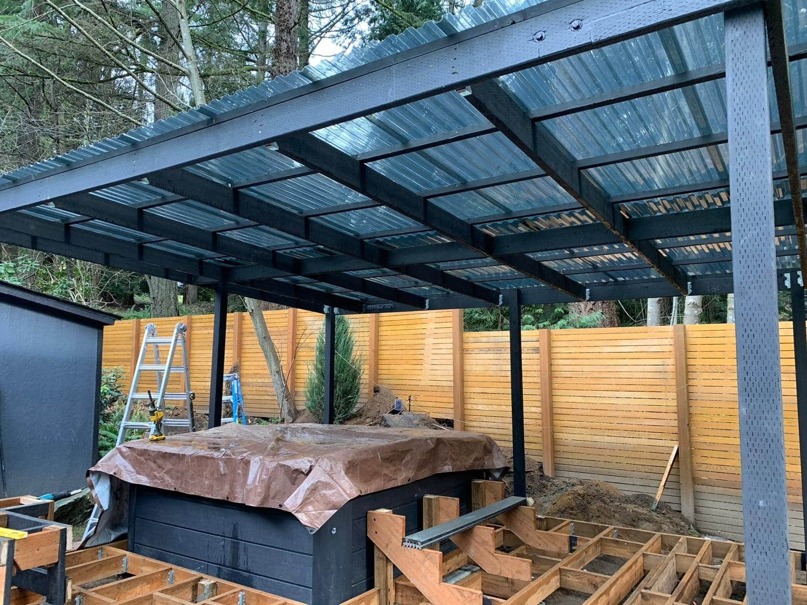 A metal and wood patio cover shades a hot tub and unfinished deck in a fenced backyard.