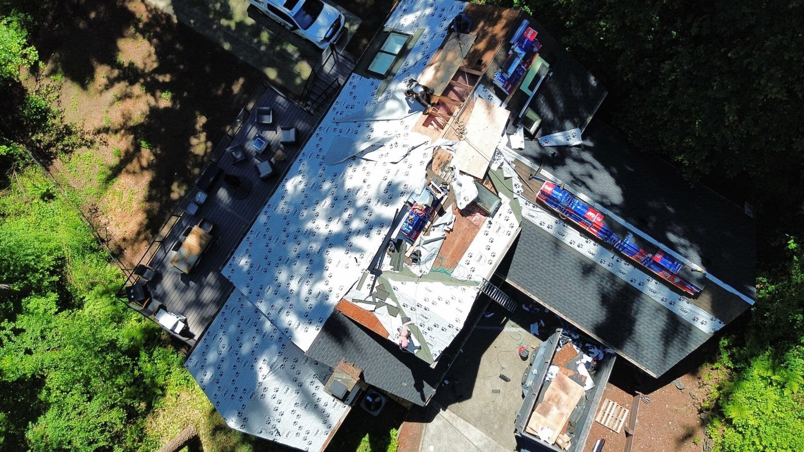 Aerial view of a residential roof repair with workers, roofing materials, and tools on the house rooftop.