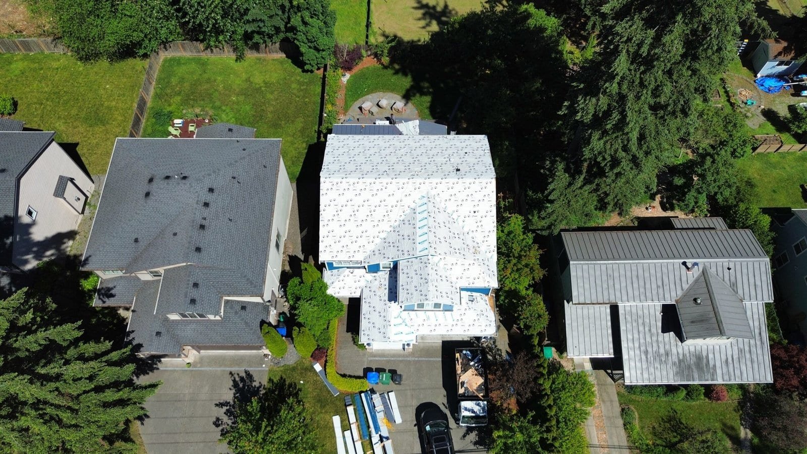 Aerial photo of three houses, featuring a central home under construction with an unfinished white roof.