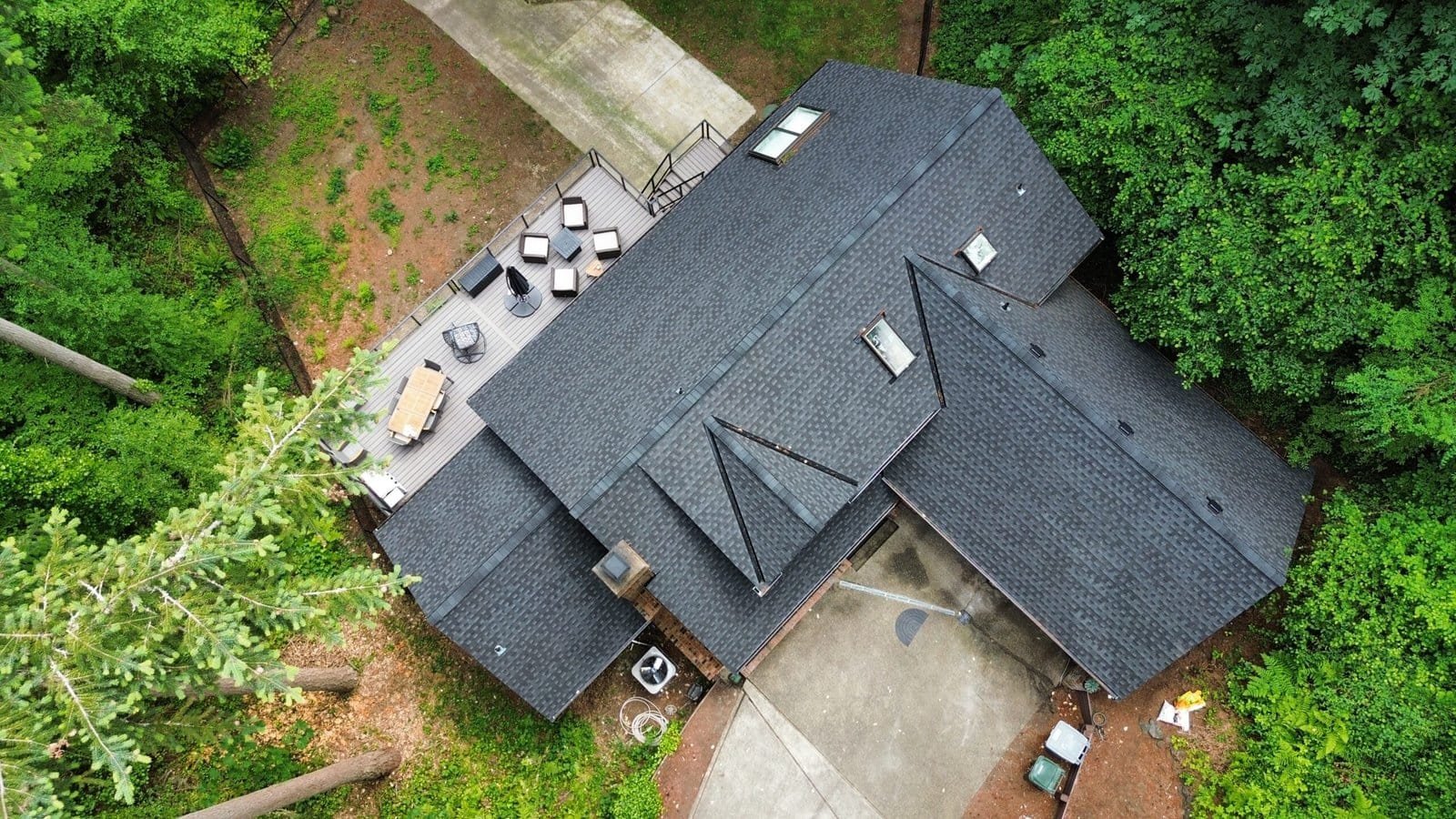 Aerial view of a house with gray roof, spacious deck, outdoor patio furniture, and mature surrounding trees.