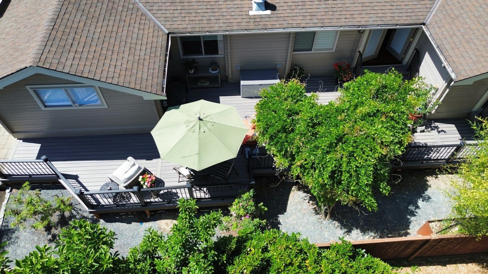 Aerial view of a backyard deck with a green umbrella, outdoor furniture, and nearby trees visible.