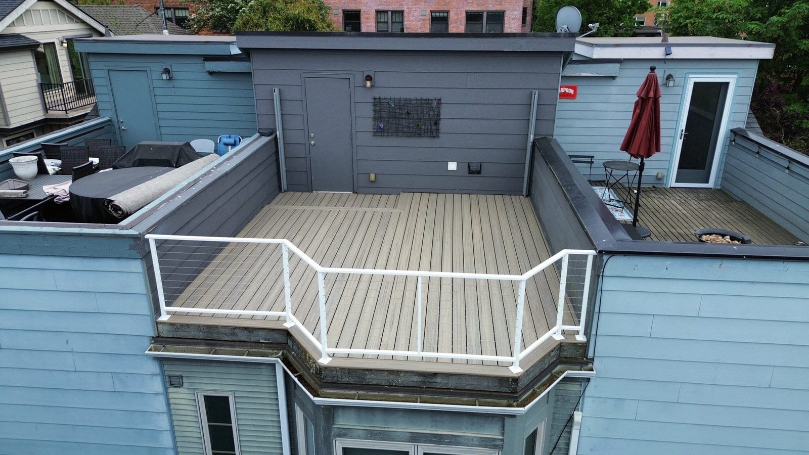 Spacious rooftop deck features patio furniture, a grill, umbrella, wood flooring, and blue-gray walls.