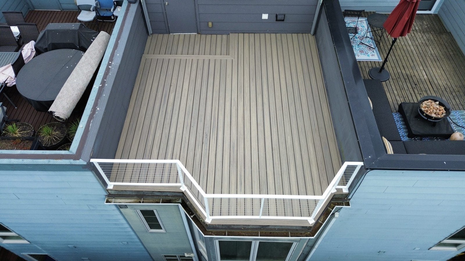 Aerial view of a rooftop deck featuring light wood flooring, gray walls, and a white safety railing.