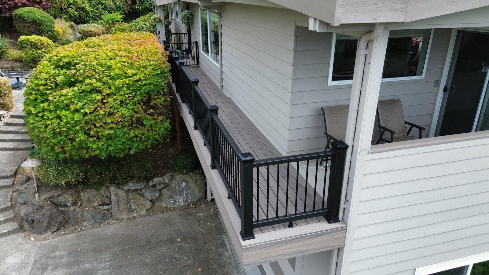 A second-story balcony features black railings, two chairs, and a nearby bush, viewed from above.