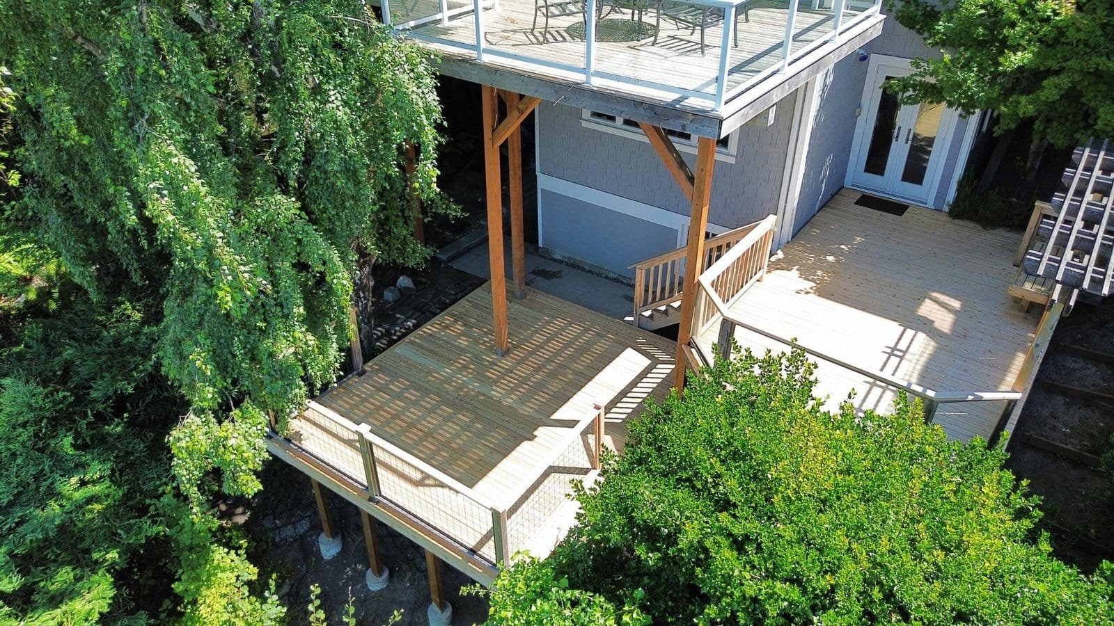 Aerial view of a wooden multi-level deck attached to a house, encircled by lush green trees.