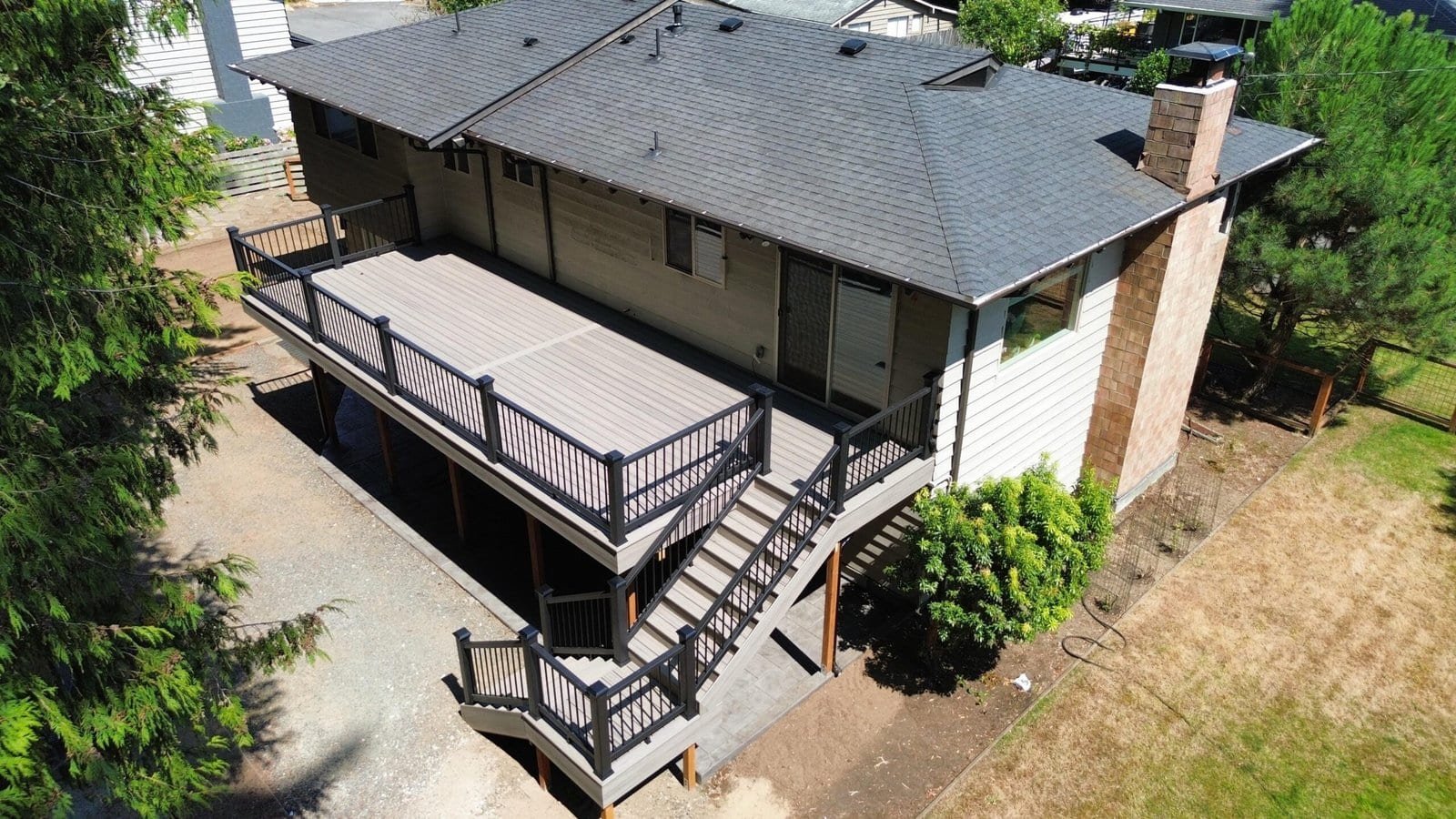A two-story house with a spacious elevated wooden deck and stairs leads to a grassy backyard area.