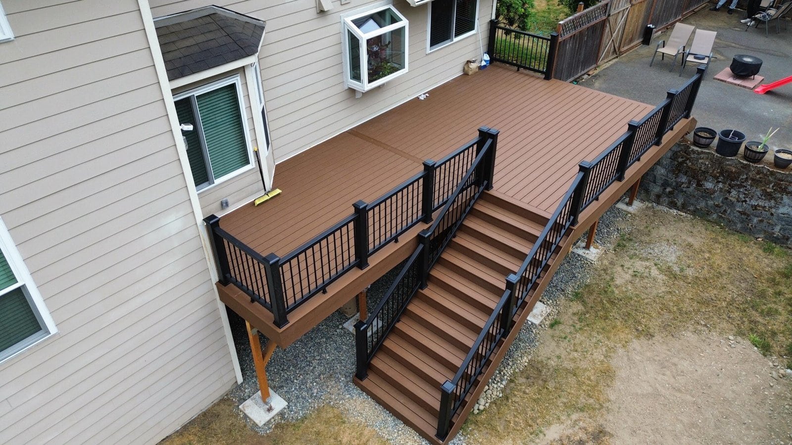 A brown backyard deck features black railings, stairs, and a broom resting on the floor of the outdoor space.