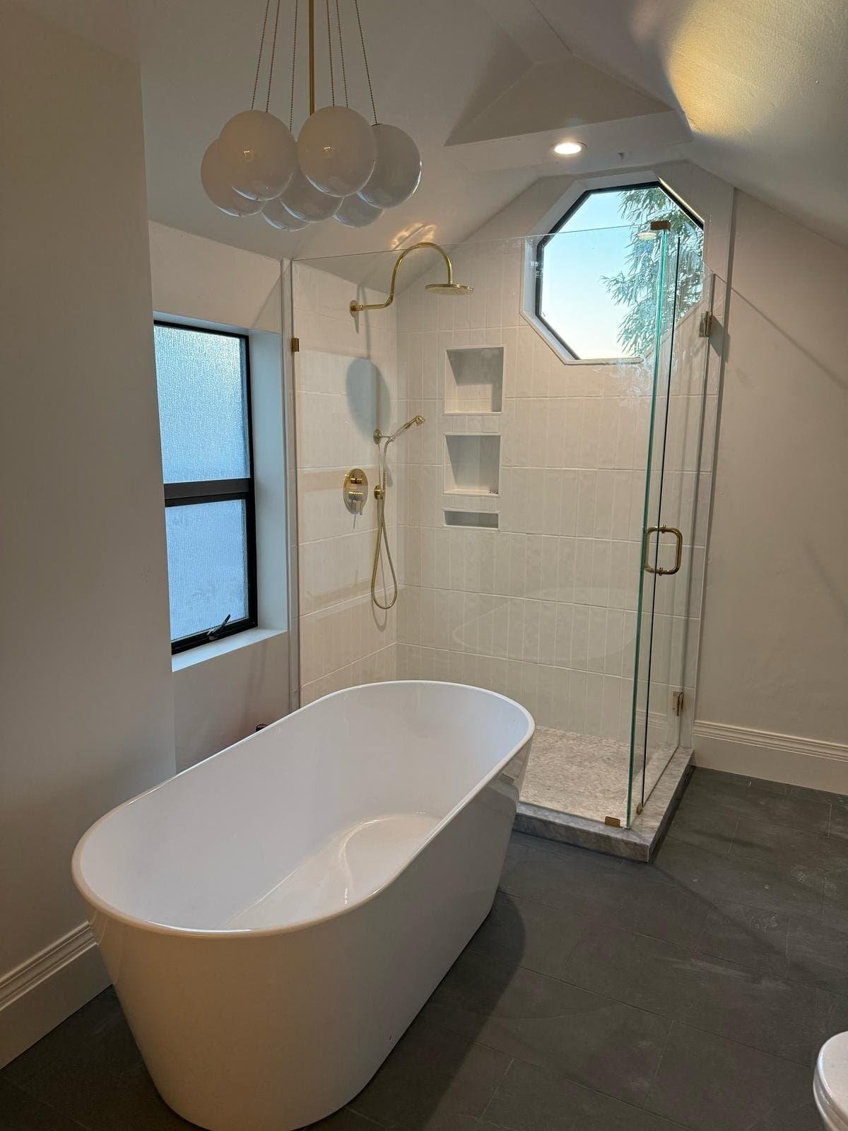 Modern bathroom featuring a freestanding tub, glass shower, gold fixtures, and a geometric window design.