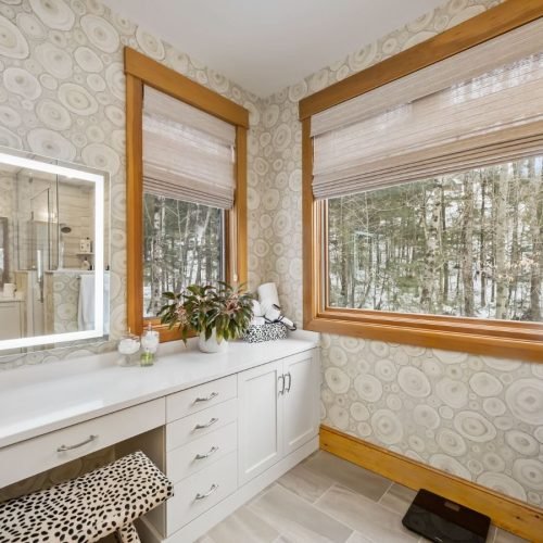 A modern bathroom featuring a vanity with a countertop and sink, positioned beneath a window that lets in natural light. The space is designed with neutral tones, clean lines, and contemporary fixtures, creating a bright and functional environment. The window adds an airy feel and illuminates the vanity area.
