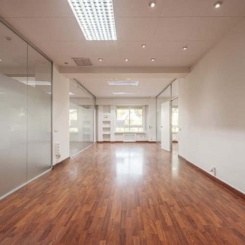 Spacious empty office with wooden floors, glass walls, and bright sunlight—perfect for flooring contractor work.