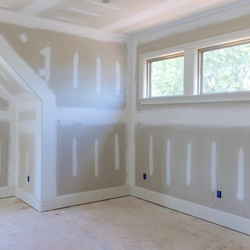 A room with unfinished drywall, white taped seams, three windows, and no flooring by a drywall contractor.