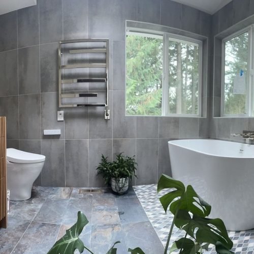 A bathroom featuring a large bathtub and a sink with a countertop and mirror. The space has tiled or painted walls and flooring, with lighting that highlights the clean and organized layout. The design emphasizes comfort and functionality for daily use.