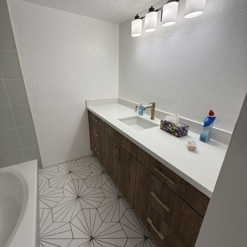 A bathroom featuring a white tiled floor and a sink with a countertop and mirror. The space is clean and well-lit, with walls that may be tiled or painted. The layout is simple and functional, creating a bright and hygienic environment.