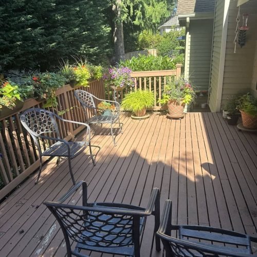 A wooden deck furnished with a table and several chairs, creating an inviting outdoor seating area. The arrangement suggests a space for dining, relaxing, or entertaining, with the deck surface and surrounding area clearly visible.