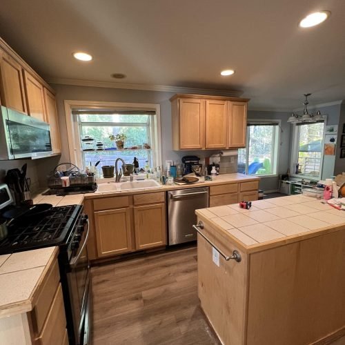 A modern kitchen featuring a spacious central island and stainless steel appliances, including a refrigerator, oven, and dishwasher. The island provides ample workspace and seating, while the bright, well-organized layout emphasizes both style and functionality.