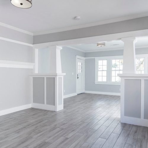 Bright, empty living room showcases fresh interior painting, gray walls, white trim, and wood-look tile floors.