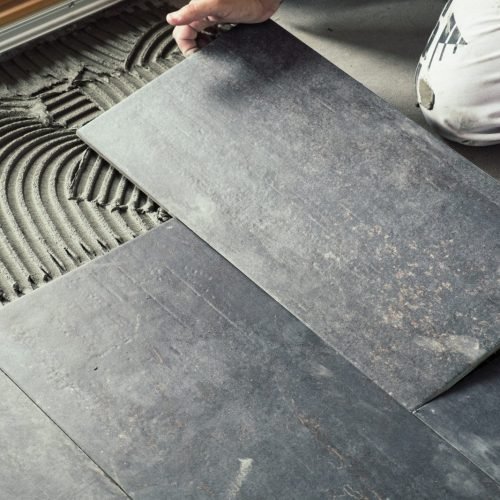 A pergola builder in Bellevue sets dark floor tiles onto adhesive, carefully aligning them for a smooth look.