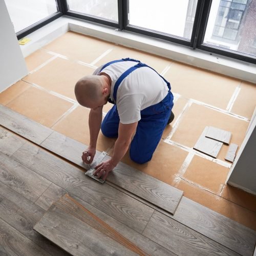 A professional kneels to install wood flooring in a sunlit room with city views in Bellevue.